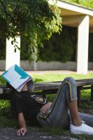 Ein Kind liegt im Schatten mit einem Buch auf dem Kopf
