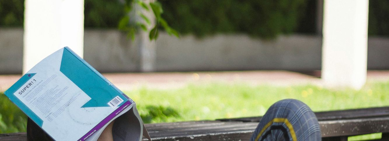 Ein Kind liegt im Schatten mit einem Buch auf dem Kopf